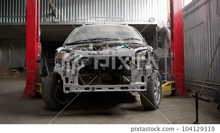 The frame of a powerful white car with body parts removed. Car bumper repair and painting. Disassembled car, in a car repair shop. The frame of a powerful white car with body parts removed. Car bumper repair and painting. Disassembled car, in a car repair shop. 104129319