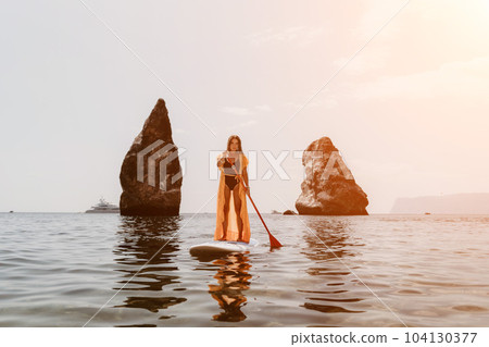 Woman sea sup. Close up portrait of happy young caucasian woman with long hair looking at camera and smiling. Cute woman portrait in bikini posing on sup board in the sea Woman sea sup. Close up portrait of happy young caucasian woman with long hair looking at camera and smiling. Cute woman portrait in bikini posing on sup board in the sea 104130377