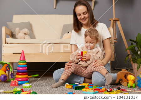 Loving Caucasian young mother and cute toddler girl playing with colorful blocks, sitting on warm floor at home, happy mum and adorable little daughter constructing tower, childcare. Loving Caucasian young mother and cute toddler girl playing with colorful blocks, sitting on warm floor at home, happy mum and adorable little daughter constructing tower, childcare. 104131017