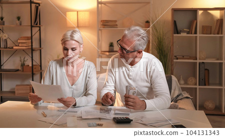 Bills payments. Family money. Couple budget. Husband wife arranging currency sitting table in light shadow room interior. Bills payments. Family money. Couple budget. Husband wife arranging currency sitting table in light shadow room interior. 104131343