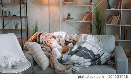 Home flu. Mobile communication. Headache suffer. Unhealthy sick woman influenza symptoms calling doctor feeling bad lying on couch home interior. Home flu. Mobile communication. Headache suffer. Unhealthy sick woman influenza symptoms calling doctor feeling bad lying on couch home interior. 104131428