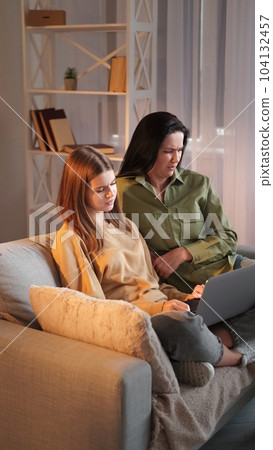 Unpleasant content. Internet browsing. Mother teen daughter watching scary movie on laptop spending evening together social media sitting sofa room interior. 104132457