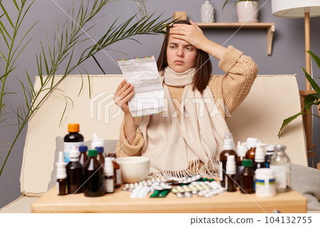 Image of unhealthy ill Caucasian woman reading instructions before taking medication, suffering terrible headache, touched her forehead, having high temperature. Image of unhealthy ill Caucasian woman reading instructions before taking medication, suffering terrible headache, touched her forehead, having high temperature. 104132755