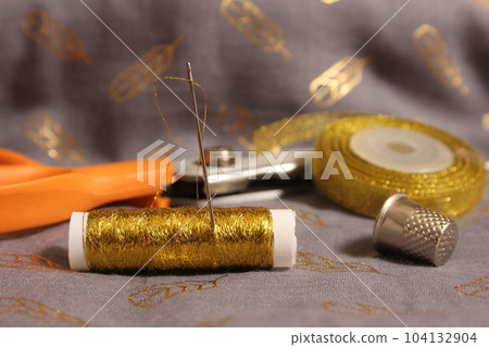 Spool of Metallic Gold Thread on Gray and Gold Chiffon Fabric 104132904