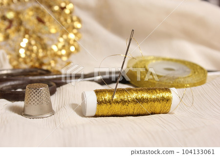 Spool of Gold Thread and Scissors With Thimble on Off White Fabric With Gold Sequins 104133061