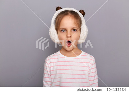 Indoor shot of shocked amazed surprised little girl standing and looking at camera with open mouth, sees something astonishing, hearing breaking news. 104133284