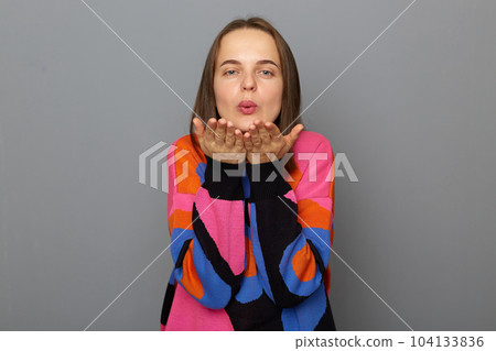 Photo of pleased attractive young woman with brown hair makes air kiss, keeps lips folded, expresses affection to close people, wearing jumper standing isolated over grey background. Photo of pleased attractive young woman with brown hair makes air kiss, keeps lips folded, expresses affection to close people, wearing jumper standing isolated over grey background. 104133836
