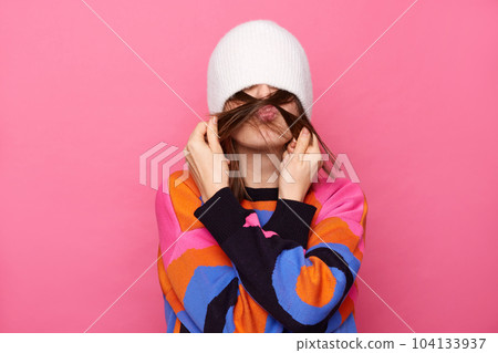 Funny childish woman with brown hair wearing sweater posing isolated over pink background, having fun with her boyfriend, pulling cap on her eyes, making mustache with hair and sending air kiss. Funny childish woman with brown hair wearing sweater posing isolated over pink background, having fun with her boyfriend, pulling cap on her eyes, making mustache with hair and sending air kiss. 104133937