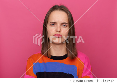 Indoor shot of sad depressed woman wearing colorful jumper posing isolated over pink background, looking at camera with pout lips, being offended, being ready to cry. 104134642