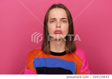 Image of sad depressed stressed woman wearing colorful jumper posing isolated over pink background, looking at camera with pout lips, being in bad mood, expressing negative emotions. 104134643