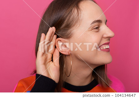 Photo of smiling satisfied woman with brown hair posing isolated over pink background, covering hand near ear, listening to somebody's private conversation, spying, showing earrings. Photo of smiling satisfied woman with brown hair posing isolated over pink background, covering hand near ear, listening to somebody's private conversation, spying, showing earrings. 104134647