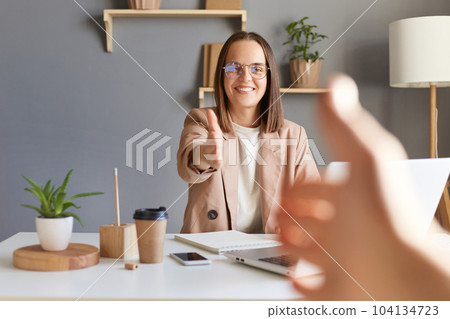 Indoor shot of attractive Caucasian smiling friendly woman freelancer working on computer, having meeting with partner, handshaking, point of view photo. 104134723