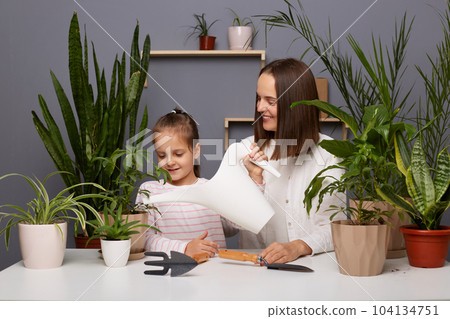 Portrait of mother and daughter take care of green plants in the room of the house, replant flowers, spend home leisure time together with pleasure. Portrait of mother and daughter take care of green plants in the room of the house, replant flowers, spend home leisure time together with pleasure. 104134751