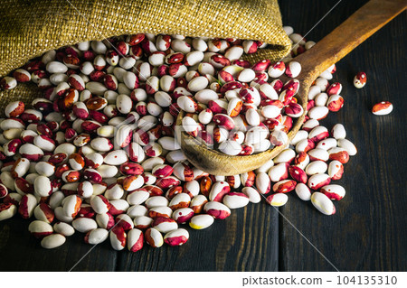 Red and white beans are poured from bag on the cooking table and a wooden spoon Red and white beans are poured from bag on the cooking table and a wooden spoon 104135310