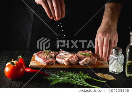 The chef sprinkles the meat with salt. Preparing meat before baking. Working environment in the kitchen of restaurant or cafe 104135396