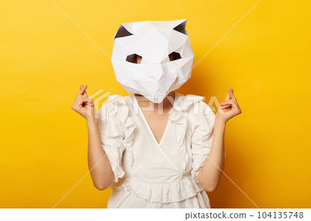 Portrait of cute unknown woman wearing dress and paper cat mask posing isolated over yellow background, standing showing mini love korean gesture, expressing romantic feelings. Portrait of cute unknown woman wearing dress and paper cat mask posing isolated over yellow background, standing showing mini love korean gesture, expressing romantic feelings. 104135748