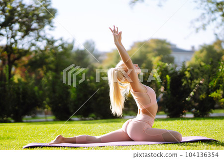 Pretty woman doing yoga exercises in the park. Portrait of woman in sportswear practicing yoga at nature. Pretty woman doing yoga exercises in the park. Portrait of woman in sportswear practicing yoga at nature. 104136354