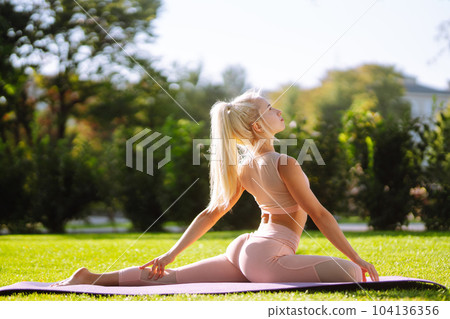 Pretty woman doing yoga exercises in the park. Portrait of woman in sportswear practicing yoga at nature. Pretty woman doing yoga exercises in the park. Portrait of woman in sportswear practicing yoga at nature. 104136356