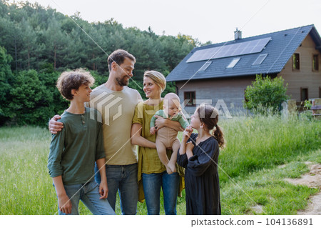 Happy family near their house with solar panels. Alternative energy, saving resources and sustainable lifestyle concept. 104136891