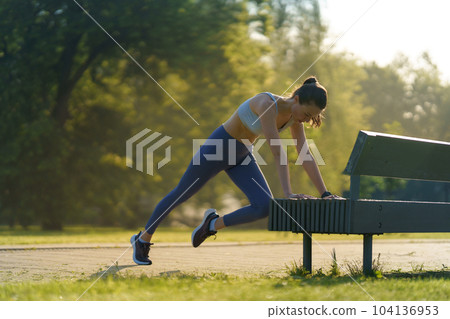 Full lenght portrait of beautiful fitness woman doing mountain clibers exercise against park bench. Full lenght portrait of beautiful fitness woman doing mountain clibers exercise against park bench. 104136953