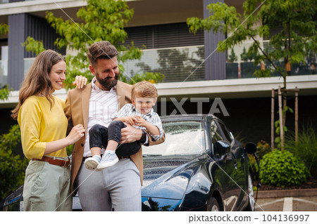 Happy family standing in front their car and charging electric car on the street. 104136997