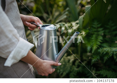 Cloe up of woman holding watering can, watering plants in a greenhouse. Cloe up of woman holding watering can, watering plants in a greenhouse. 104137178