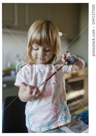 Cute little girl painting on her own hand with tempera paint,. 104137500