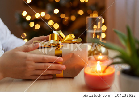 Profile portrait of faceless unknown female holding gift box with gold bow and ribbons in hands, preparing for New Year and Christmas holidays, wants to to congratulate closed people. 104138622
