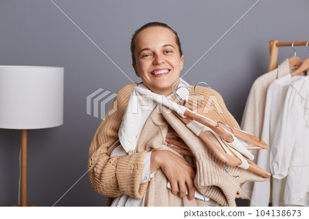 Portrait of young adult woman shopper holding clothes on racks in modern boutique, embracing her new attires, being happy to do shopping, enjoying her new clothing, buying outfits in showroom. Portrait of young adult woman shopper holding clothes on racks in modern boutique, embracing her new attires, being happy to do shopping, enjoying her new clothing, buying outfits in showroom. 104138673