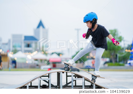 Child or kid girl playing surfskate or skateboard in skating rink or sports park at parking to wearing safety helmet elbow pads wrist and knee support Child or kid girl playing surfskate or skateboard in skating rink or sports park at parking to wearing safety helmet elbow pads wrist and knee support 104139029