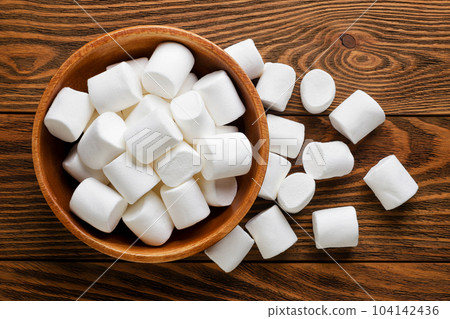 Marshmallows in a plate and scattered on a wooden background. Top view 104142436