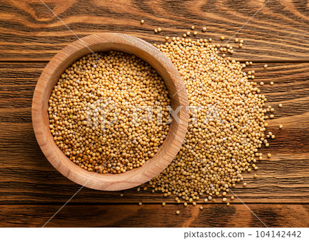 Mustard grains in a plate and scattered on a wooden background. Top view 104142442