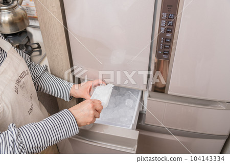 [一位家庭主婦將冰塊放入製冰機的玻璃杯中] 104143334