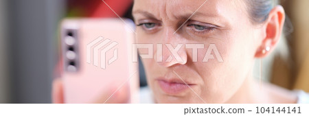 Closeup portrait of woman looking at smartphone display closely with eye problems Closeup portrait of woman looking at smartphone display closely with eye problems 104144141