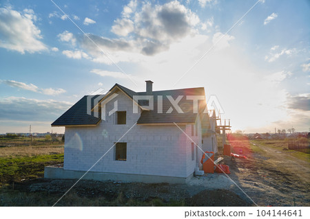 Aerial view of unfinished house with aerated lightweight concrete walls and wooden roof frame covered with metallic tiles under construction. 104144641