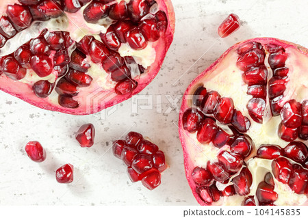 Pomegranate halves, gem like fruits scattered on white board, photo from above. 104145835