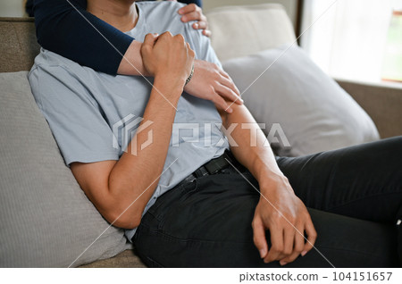 Cropped image of a happy gay couple hugging each other on a couch in the living room. Cropped image of a happy gay couple hugging each other on a couch in the living room. 104151657