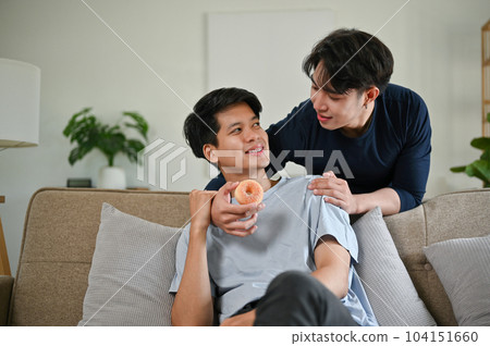 A handsome Asian gay man feeds a doughnut to his boyfriend. LGBTQ+, relationship, homosexual A handsome Asian gay man feeds a doughnut to his boyfriend. LGBTQ+, relationship, homosexual 104151660