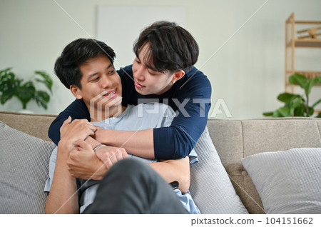 A happy and carefree Asian male gay couple hugging each other while relaxing in the living room 104151662