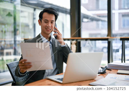 A professional Asian businessman is looking at the details on report and talking on the phone A professional Asian businessman is looking at the details on report and talking on the phone 104152725