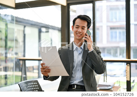 A professional Asian businessman is looking at the details on report and talking on the phone A professional Asian businessman is looking at the details on report and talking on the phone 104152726