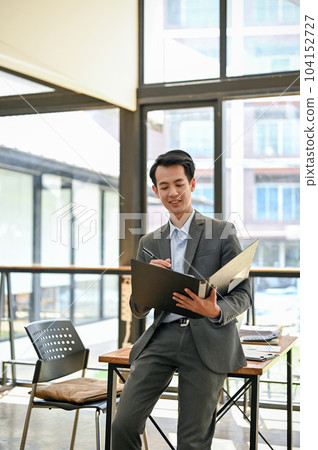 A smart Asian businessman checking business report in a document folder in his office. A smart Asian businessman checking business report in a document folder in his office. 104152727