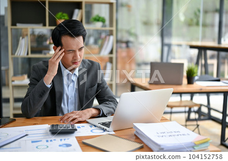 A stressed and thoughtful Asian businessman is working at his desk in the office. 104152758