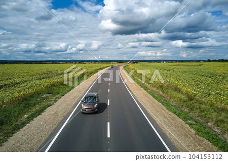 Aerial view of intercity road between green agricultural fields with fast driving car. Top view from drone of highway traffic Aerial view of intercity road between green agricultural fields with fast driving car. Top view from drone of highway traffic 104153112