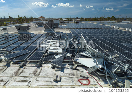 Aerial view of damaged by hurricane wind photovoltaic solar panels mounted on industrial building roof for producing green ecological electricity. Consequences of natural disaster 104153265