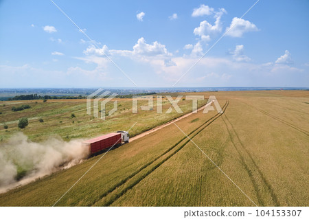 Aerial view of cargo truck driving on dirt road between agricultural wheat fields making lot of dust. Transportation of grain after being harvested by combine harvester during harvesting season 104153307