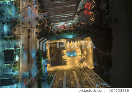 Aerial view of brightly illuminated high skyscraper hotel in downtown district in Sunny Isles Beach city in Florida, USA. Swimming pools and tourist infrastructure in Florida resort 104153316