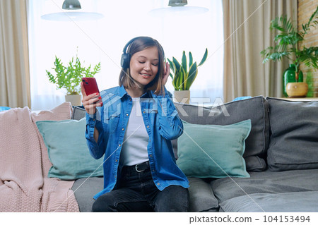 Young woman in headphones listening music, sitting on sofa at home 104153494