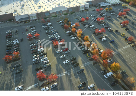 Aerial view grocery shopping mall and many colorful cars parked on parking lot with lines and markings for parking places and directions. Place for vehicles in front of a strip mall plaza 104153878