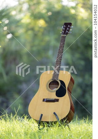Acoustic guitar outdoors on greenery background. Concept of calm music Acoustic guitar outdoors on greenery background. Concept of calm music 104154012